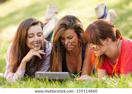 Photo of three woman sitting on grass while looking at a digital screen
