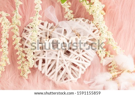 Home decoration on pink fur background. Wooden heart with ribbon and word home, white flowers and feathers closeup picture.