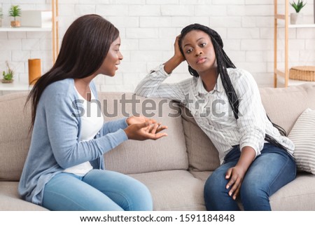 Indifference in friendship. Bored black girl tired of listening her talkative girlfriend while sitting on sofa at home together Royalty-Free Stock Photo #1591184848