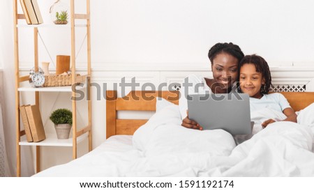 Happy Loving Family. Black mom and daughter watching video on laptop, lying in bed together. Copy space, panorama