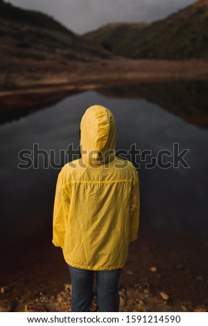 One person facing away of the camera with a yellow oilsking hoodie looking at a red river in Spain. Photography