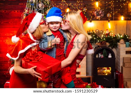 Happy cute child in Santa hat with sisters have a Christmas. Little Santa Claus gifting gift. Happy kid having fun with gift
