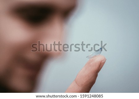 Close up picture of contact lens on a mans finger. Face in the blurry background.