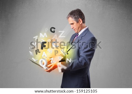 Middle aged businessman in suit holding laptop with colorful letters