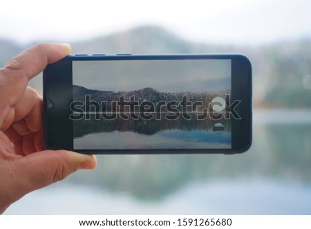 Man hold Smart phone and photo shoot landscape on Alpsee. Germany, Bavaria. Hand holding black smartphone taking a photo of mountain and lake. focus on screen. 