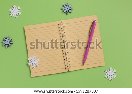 Open notebook and snowflakes, on green background. Flat lay, top view, copy space.