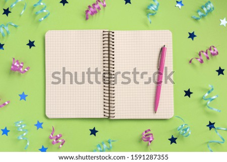 Open notebook, colorful serpentine and stars, on green  background. Flat lay, top view, copy space.