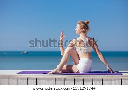 Sporty young woman doing stretching sitting in Half lord of the fishes, Ardha Matsyendrasana pose. Slim girl practicing yoga outdoor, blue sky, white wooden terrace. Relax, healthy lifestyle concept