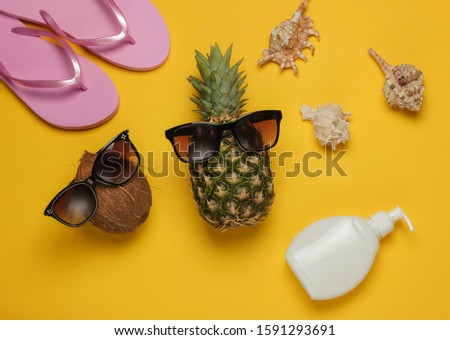 Summer background. Fun and humor. The concept of a beach holiday, travel. Pineapple and coconut
with sunglasses, beach accessories on yellow background. Top view