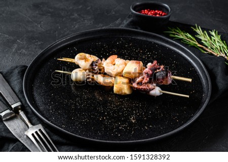 Wooden skewers with shrimp, octopus, squid and mussels. Kebab with seafood. Black background. Top view