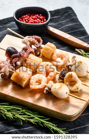 Wooden skewers with grilled seafood, shrimp, octopus, squid and mussels. Gray background. Top view