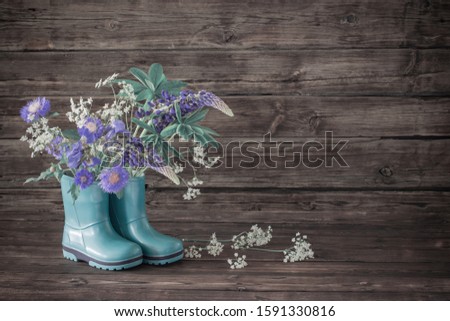 summer flowers in rubber boots on old dark wooden background