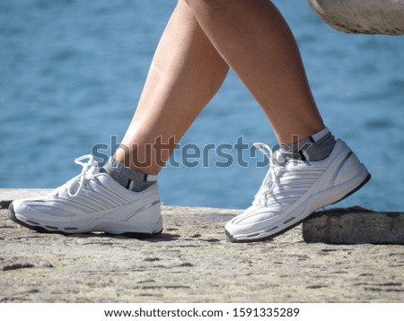 Women legs in white shoes sitting near the water. Concept of journey travel, active life or sport background. Royalty-Free Stock Photo #1591335289