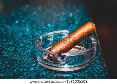 A closuep shot of a cigar in an ashtray with blurred turquoise background