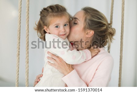 Loving and friendly family. Emotional portrait of a tender and positive beautiful young woman kissing her little smiling blonde daughter blonde relaxing on the bed in the bedroom.Happy childhood