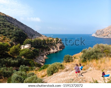 Beautiful aerial view of hiker couple look to distance. mountains and sea on sun rise. Trail for active sports, hiking to a wild beach, tourist destination. Ieranto bay, Nerano, Massa Lubrense, Italy