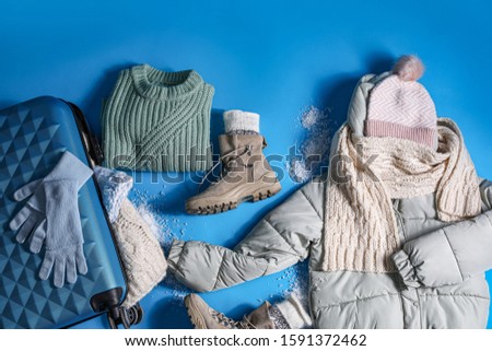 Suitcase with warm clothes on light blue background, flat lay. Winter vacation