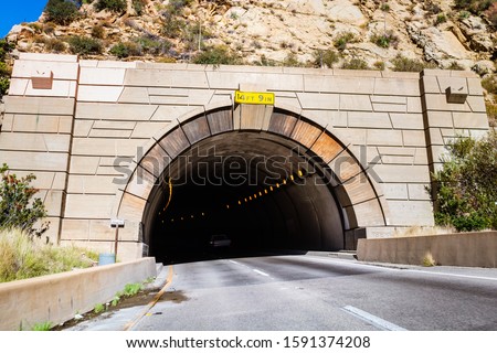 Tunnel carved into a mountain on Highway 1, California; maximum height displayed at the entrance; highway skewing left due to road curve