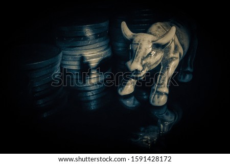 Bull figurine on a black reflective surface on a background of coins.The symbol of the upward trend.
