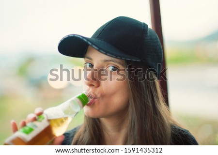 Young woman is drinking a beverage from a glass bottle