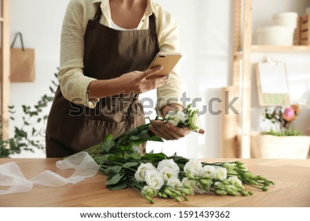 Florist taking picture of beautiful flowers in workshop, closeup
