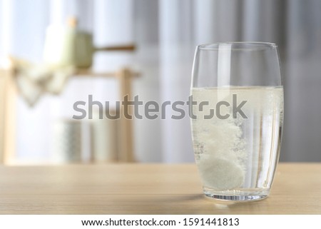 Glass of water with effervescent tablet on wooden table indoors, space for text