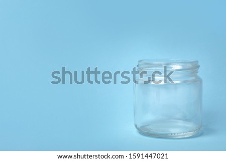Open empty glass jar on light blue background, space for text