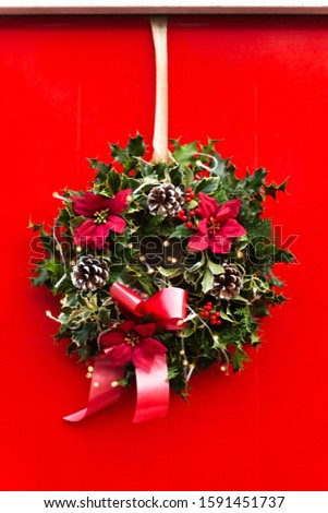 Amazing Christmas wreath with big red bow, Red Christmas Poinsettia flowers and Holly Berries on red door, Xmas celebration concept