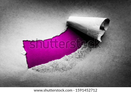 A hole in vintage paper with torn edges close-up with a pink vibrant color background inside.