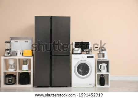 Modern refrigerator and other household appliances near beige wall indoors Royalty-Free Stock Photo #1591452919