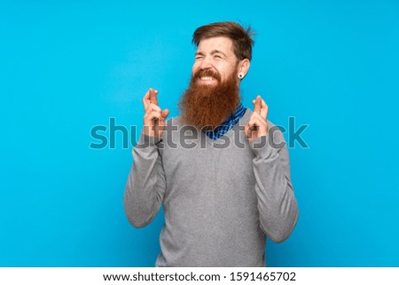 Redhead man with long beard over isolated blue background with fingers crossing and wishing the best