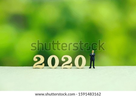 Miniature people - businessman greeting for happy new year 2020 with dreamy green background