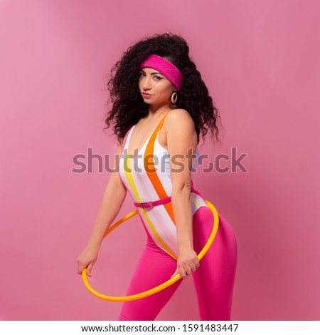 Photo of slim woman 80s wearing aerobic clothes doing exercises with hula hoop during gymnastics against pink wall