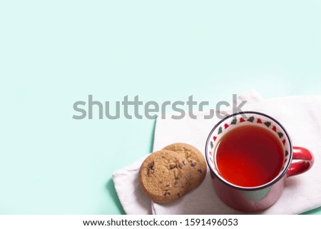 red Christmas mug with Christmas trees with black tea and homemade cookies on a napkin on a light background, close-up, top view