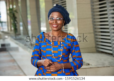beautiful african woman in traditional clothes standing outdoors looking at camera smiling.