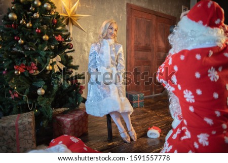 Santa Claus takes pictures and having fun near the Christmas tree and the beautiful Snow Maiden