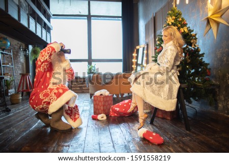 Santa Claus takes pictures and stands near the Christmas tree and the blonde Snow Maiden