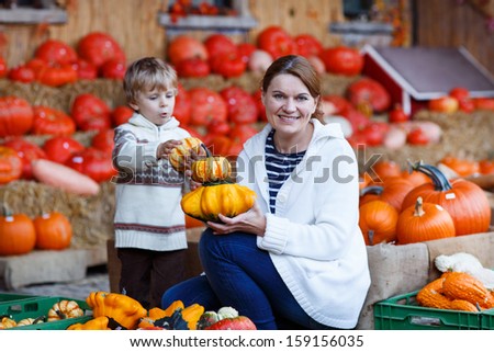 Young mother and her little son playing on pumpkin patch farm. Selective focus on woman.