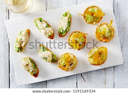 Food photography of canape' selection photographed overhead: pea artichoke bruschetta and fetta leek tartlets on a white serving platter, white rustic table top background 