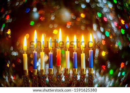 Menorah with burning candles for Hanukkah on sparkle background with defocused colorful lights. Jewish holiday.