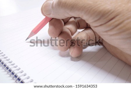 A hand with a pencil and a spiral notebook with a blank page - Copy space