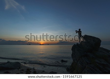 
Silhouette of photographer shooting a sunset. A man with a camera stands on the rocks and shoots a beautiful sunset over the sea.