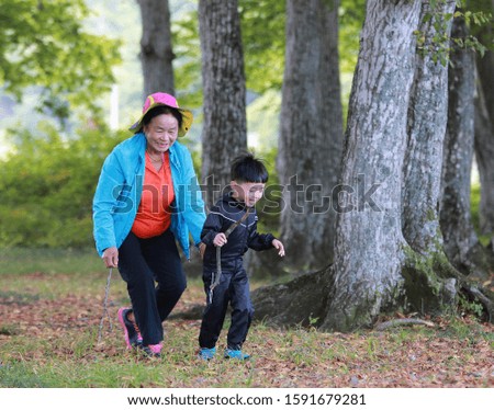 A picture of an old lady and her grandson playing in a tree park.