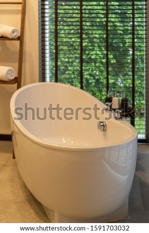 blurred background, A ceramic bathtub with two faucets located in a bathroom. there are Shampoo, Bath and Shower Gels placed near a bathtub