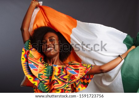 Happy african woman in national clothes smiling and posing with a flag Ivory Coast, C te d'Ivoire isolated over a gray background Royalty-Free Stock Photo #1591723756