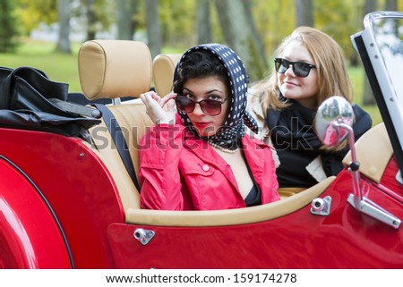 Fashionable women at retro red car look satisfied