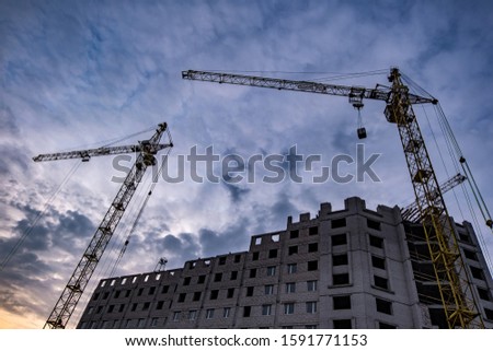 Tower cranes and unfinished multi-storey high buildings under construction site in the evening with dramatic colorful cloud background