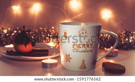 White mug with the inscription merry christmas and golden patterns, candles, cookies and mandarin.