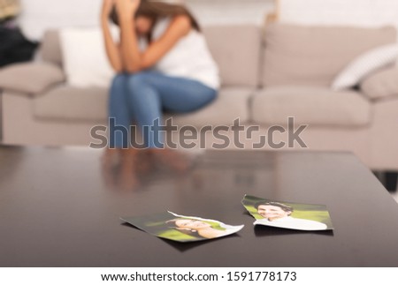 Unrecognizable Woman Crying After Breakup With Ex Boyfriend Sitting On Sofa Indoor, Torn Apart Photo Of Couple Lying On Table