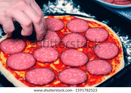The application of salami on the pizza dough. Cooking pizza. The cook lays out the filling on the dough. Homemade pizza.